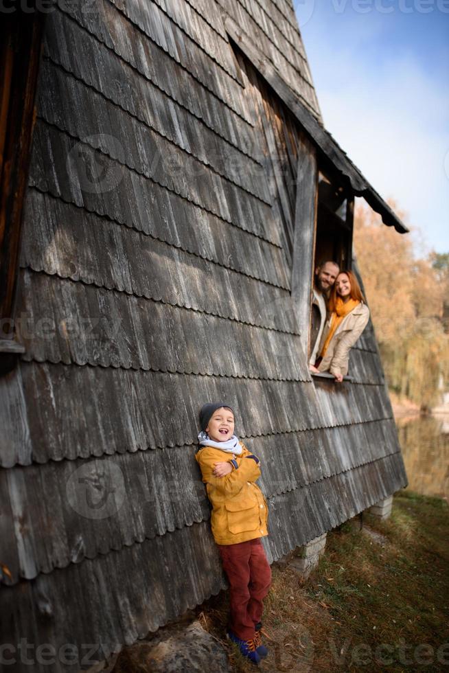 feliz familia joven asomándose por las ventanas de una gran casa de madera. el concepto de comprar una casa, alquilar una casa, para una familia foto