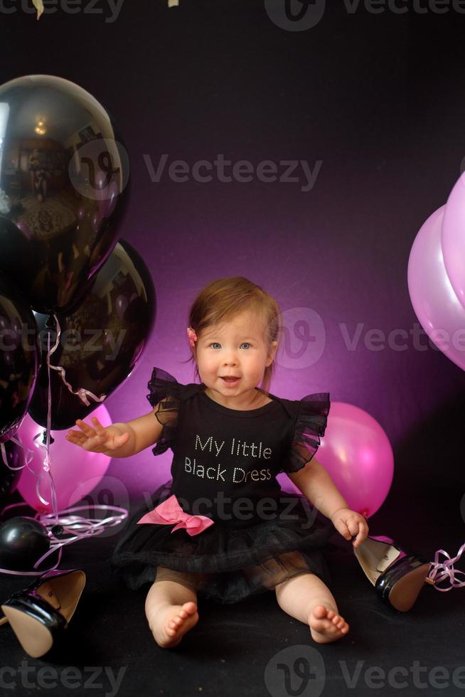 día de la fiesta de cumpleaños de la niña del primer año. globos y vacaciones en interiores. cumpleaños del niño niña bonita en su primer vestido negro foto