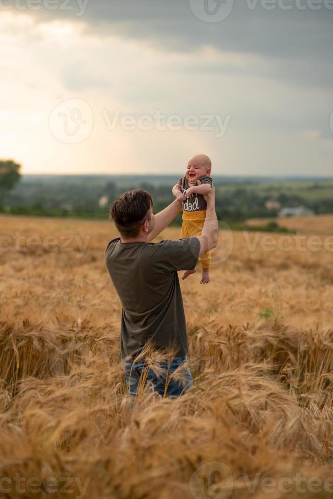 A young father holds his three month old son in his arms. Filmed in a wheat field. photo
