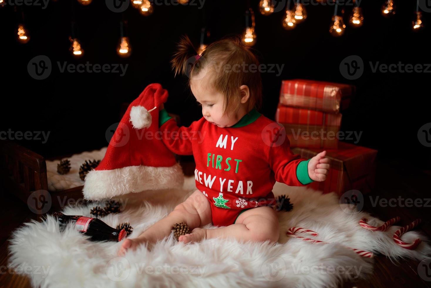 7 month old girl in a red Christmas costume on a background of retro garlands sits on a fur photo