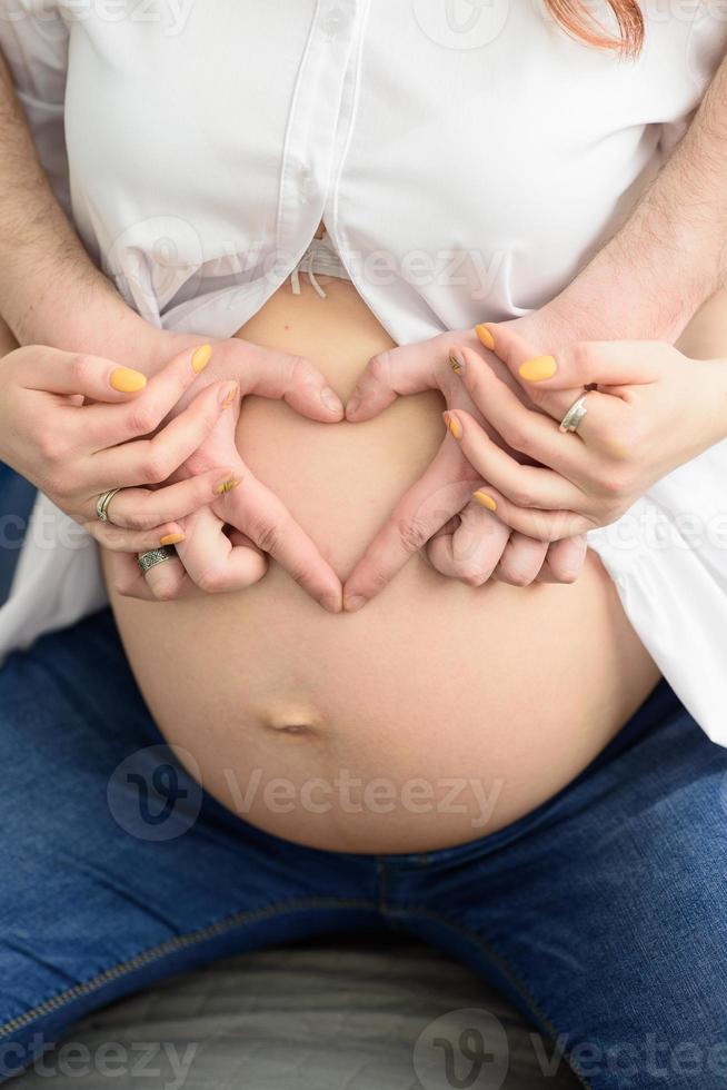 Future father shows fingers heart on the belly of his pregnant wife photo