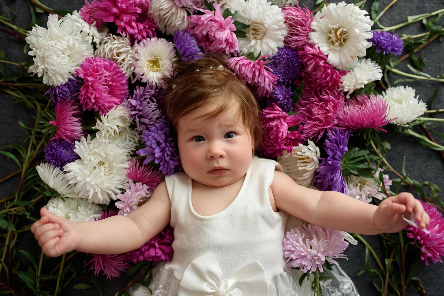 Baby girl in blue dress playing with bunch of pink tulips. Little child at home in sunny nursery. Toddler having fun with flowers photo