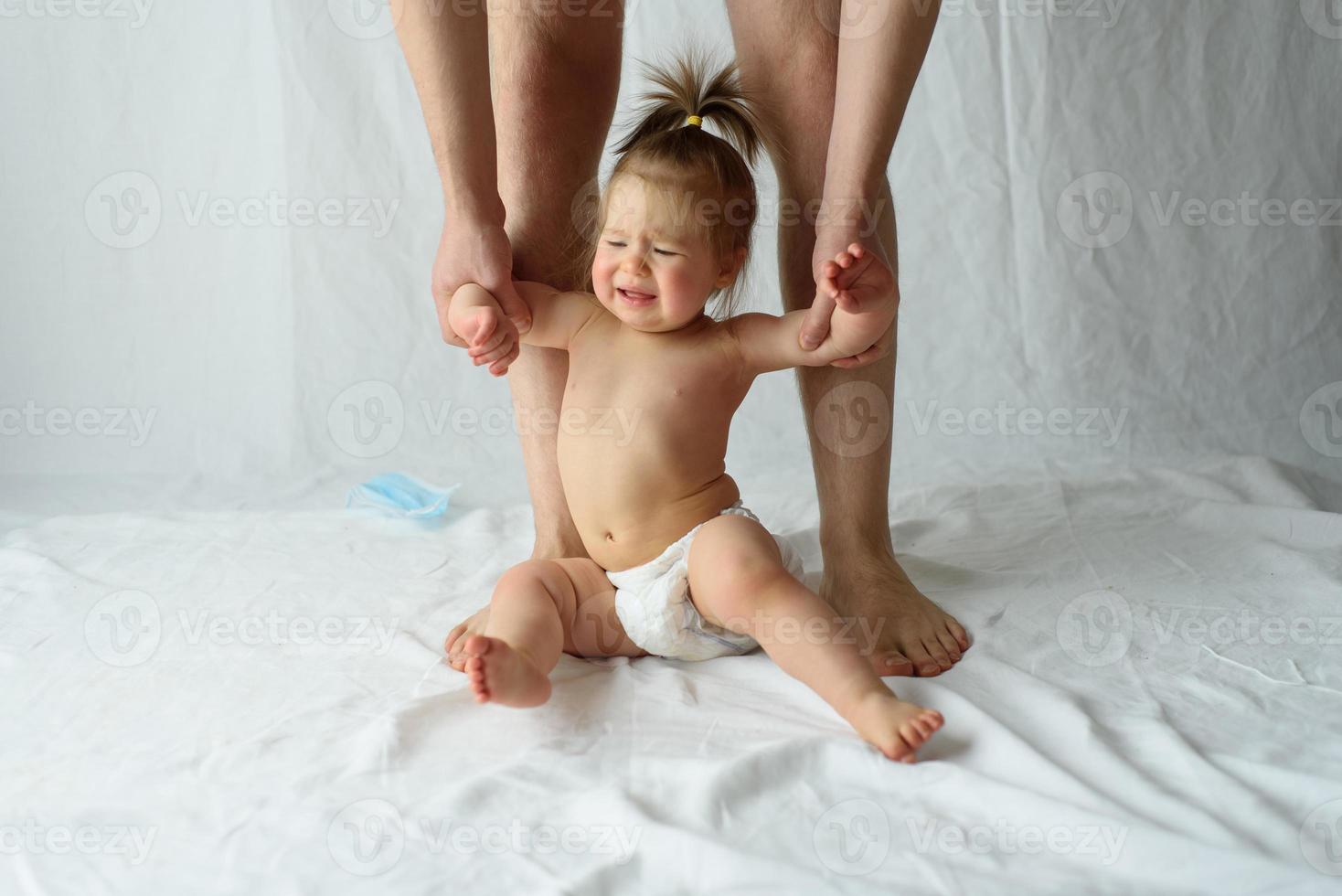 little girl crying on a white background. Hands of the father hold the child. photo