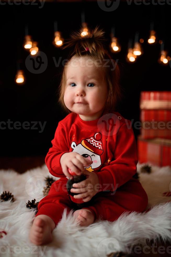 7 month old girl in a red Christmas costume on a background of retro garlands sits on a fur photo