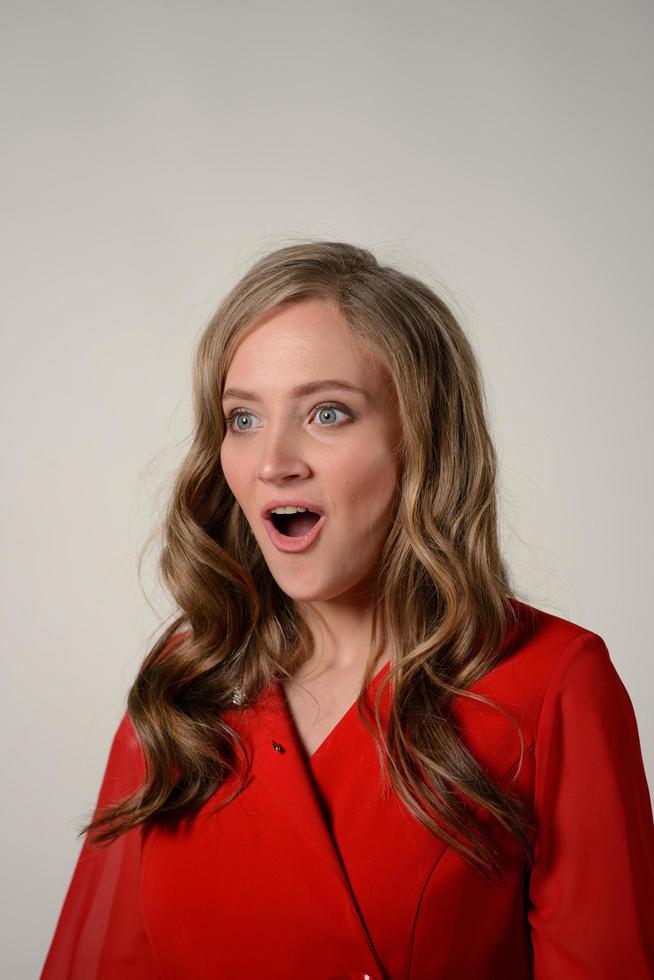 Portrait of a happy young woman dressed in red dress pointing fingers up at copy space photo