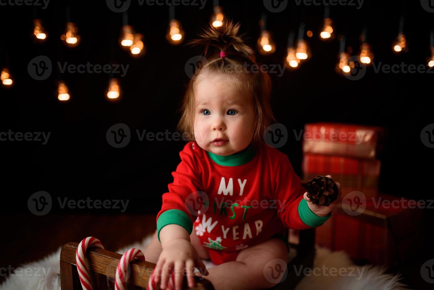 7 month old girl in a red Christmas costume on a background of retro garlands sits on a fur photo