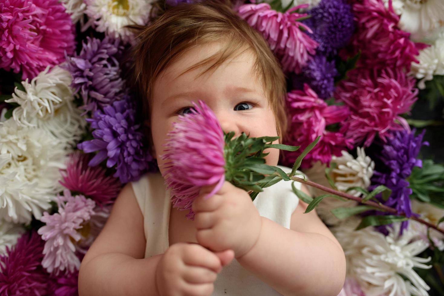 niña en vestido azul jugando con ramo de tulipanes rosas. niño pequeño en casa en la guardería soleada. niño divirtiéndose con flores foto