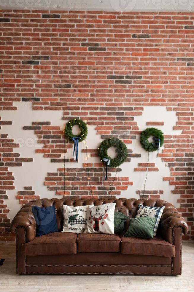 elegante interior de salón navideño en estilo loft con sofá marrón, coronas y guirnaldas. tiempo familiar. plantilla. foto