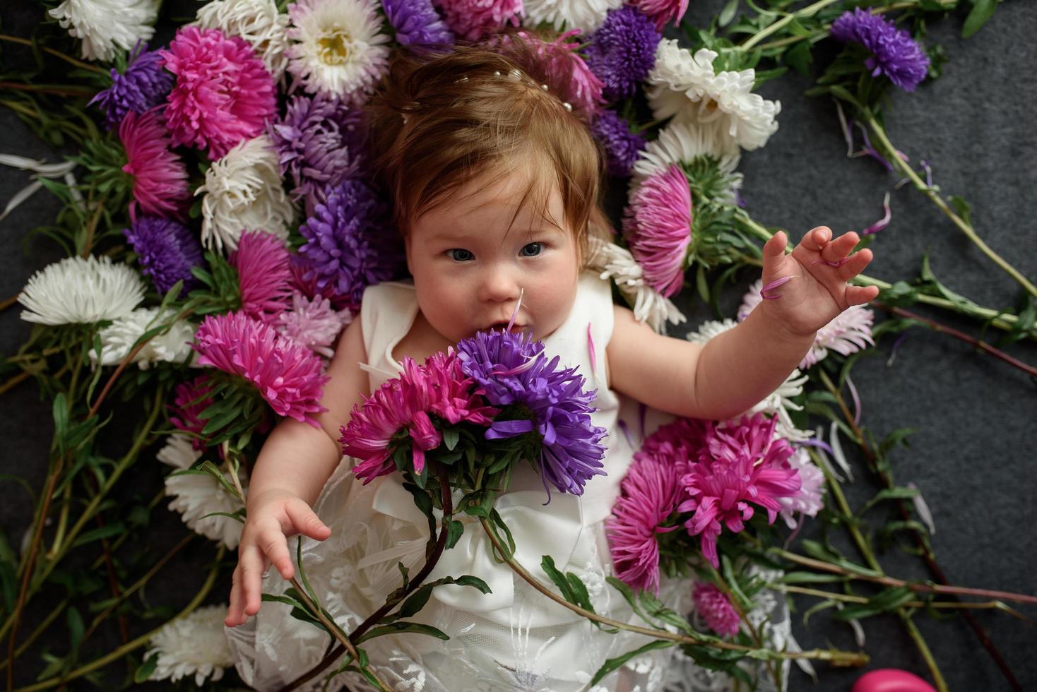 Baby girl in blue dress playing with bunch of pink tulips. Little child at home in sunny nursery. Toddler having fun with flowers photo