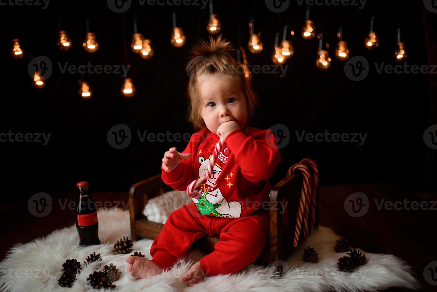 7 month old girl in a red Christmas costume on a background of retro garlands sits on a fur photo