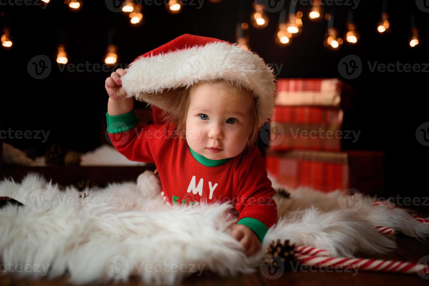 7 month old girl in a red Christmas costume on a background of retro garlands sits on a fur photo