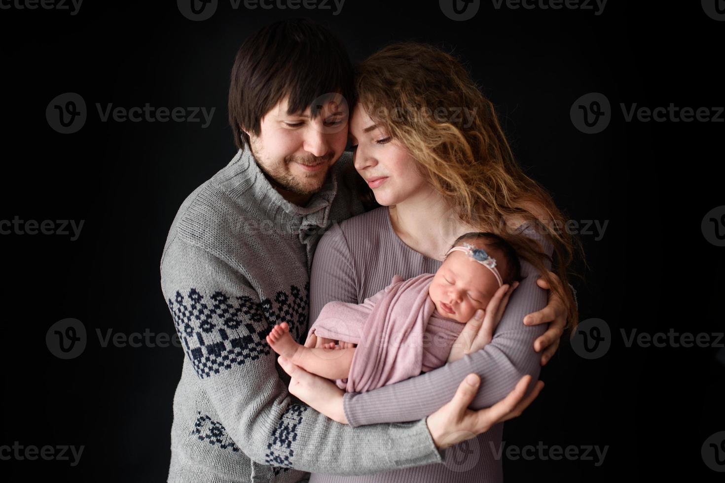 Parents are holding their newborn daughter. Picture taken on a dark background. photo