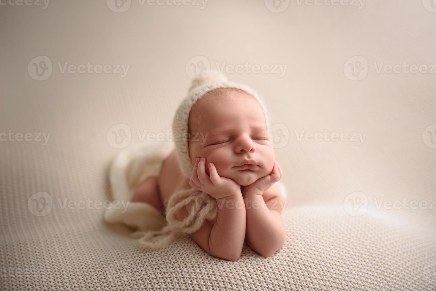 Newborn baby boy in a knitted hat sleeps on a light knitted blanket. photo