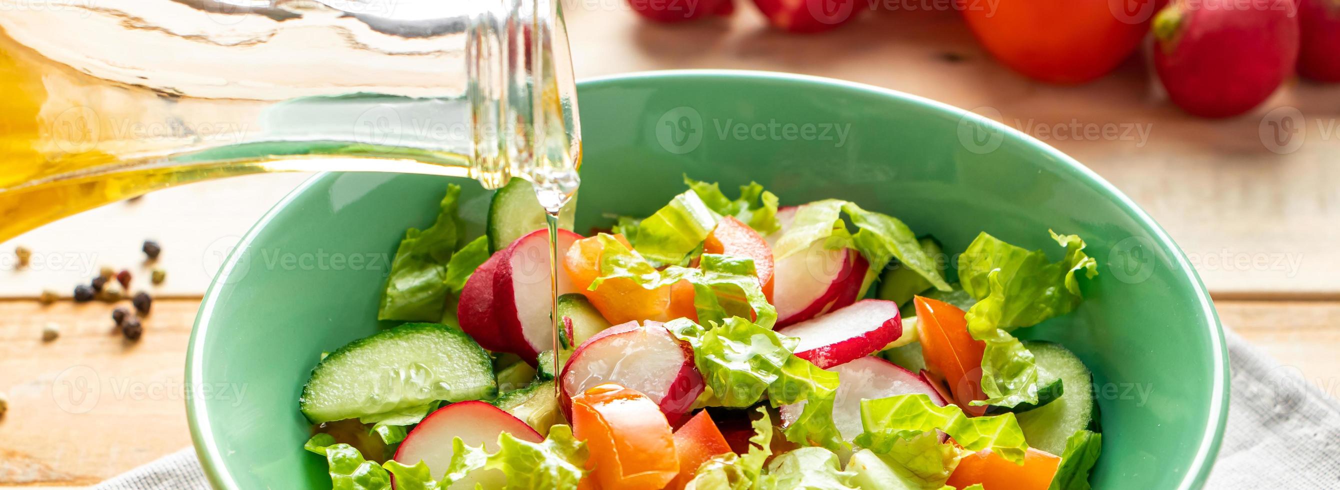 Ensalada de verduras frescas con aceite de oliva en un tazón de cerámica sobre fondo de madera. foto