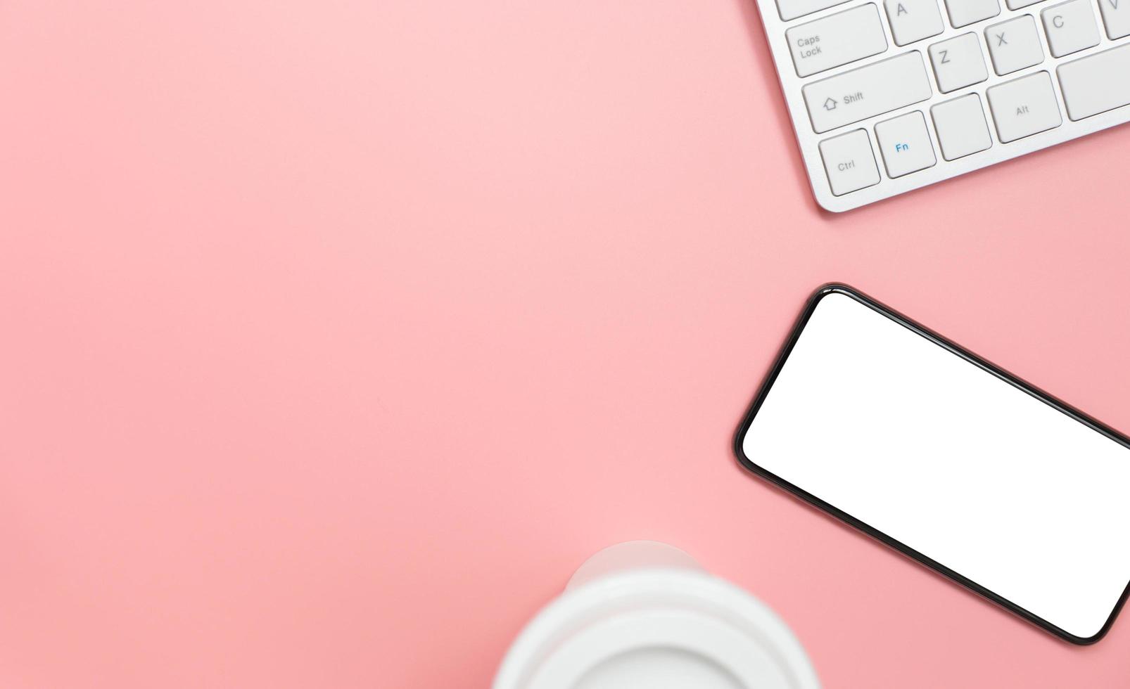 Top view with copy space of Computer keyboard smartphone and coffee mug overhead on pink pastel background, Flat lay concept photo