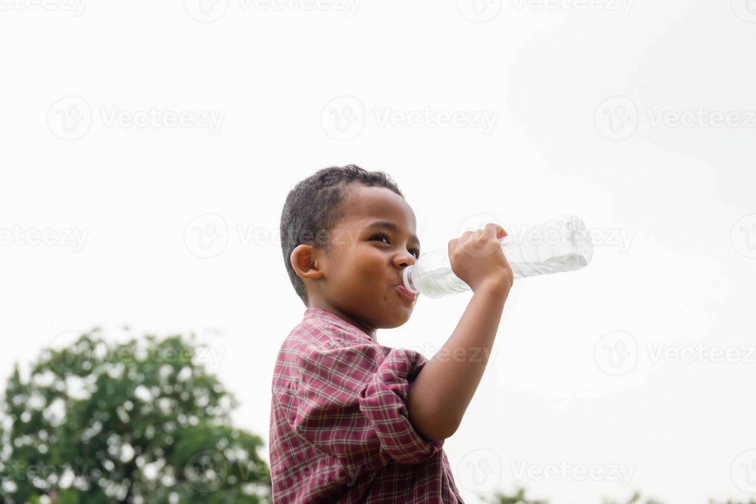 Cheerful african american boy drinking water after playing at park photo