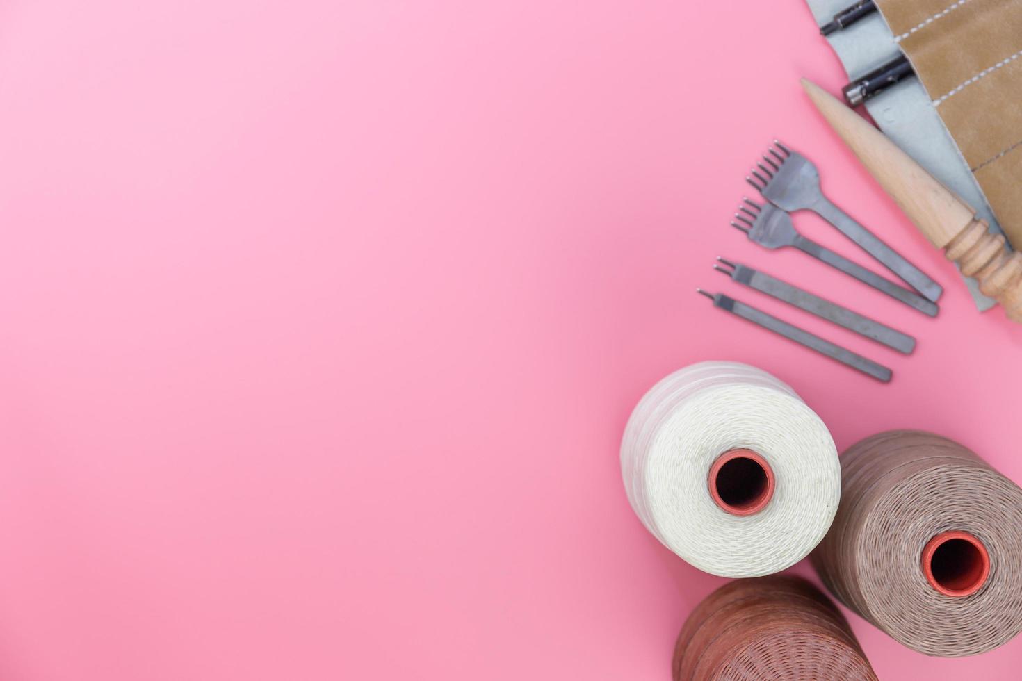 Top view with copy space of leather craft tools group, waxed rope, diamond hole punch and shape punch overhead on pink pastel background, Leather craft or leather working flat lay concept photo