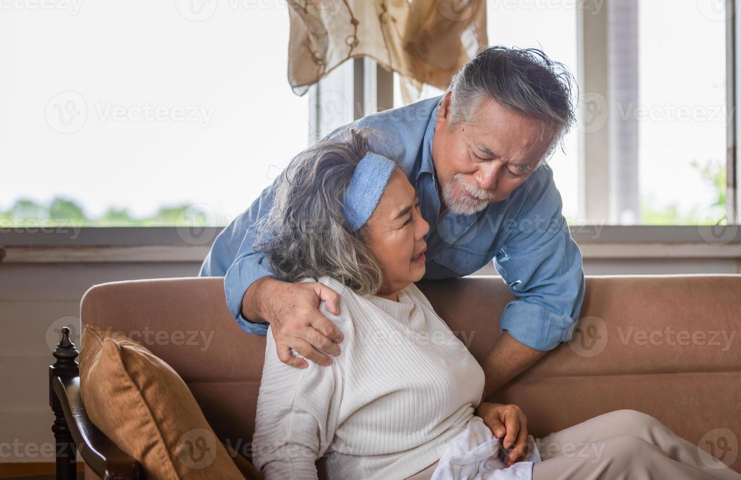 Elderly asian carrying his wife in pain lying on sofa in living room at home, family health care and support concept photo