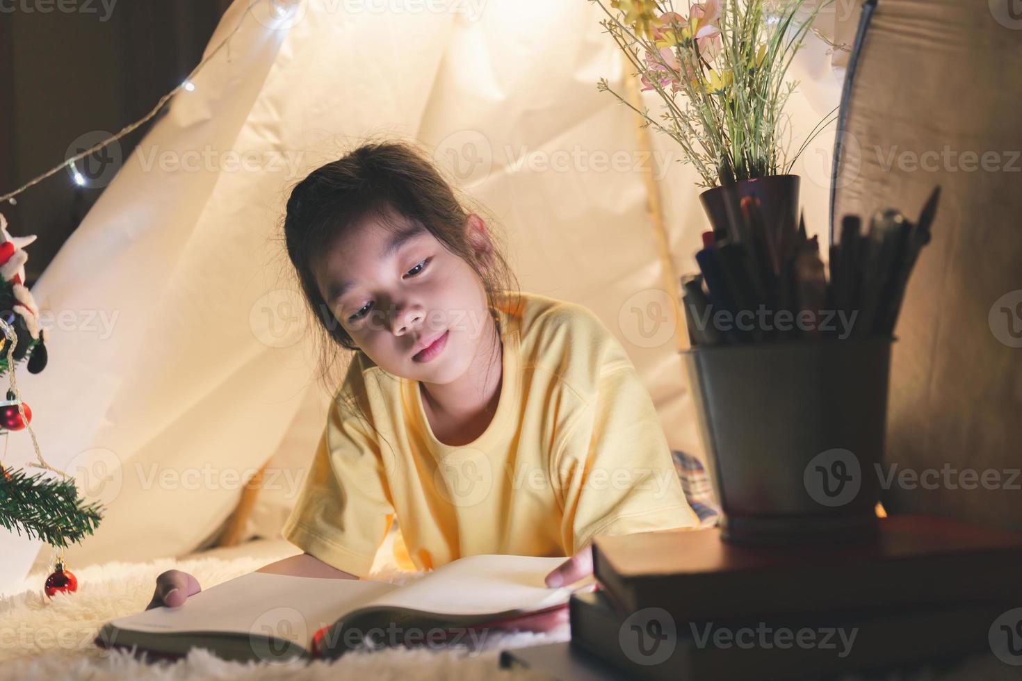 niña leyendo un libro en la tienda, niño feliz jugando en casa, niño divertido y encantador divirtiéndose en la habitación de los niños. foto