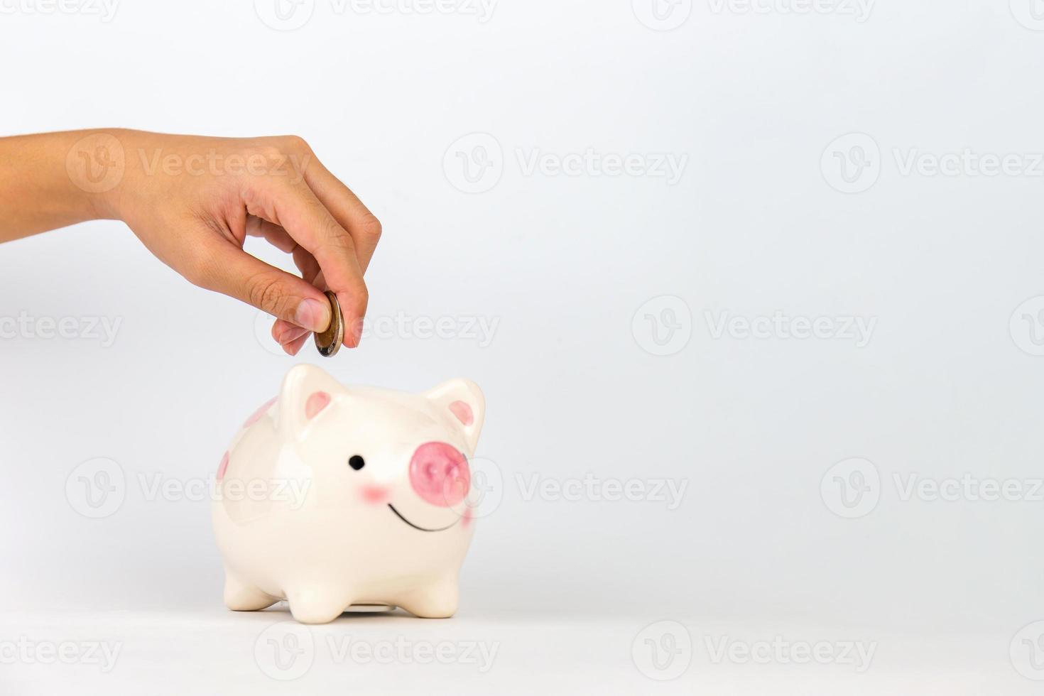 mano poniendo moneda en la hucha sobre fondo blanco, ahorrando conceptos foto