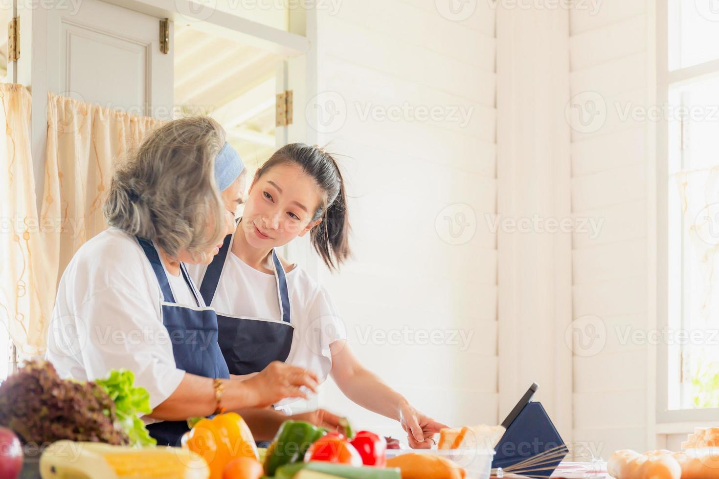 Middle aged daughter and senior asian mother cooking together at kitchen photo
