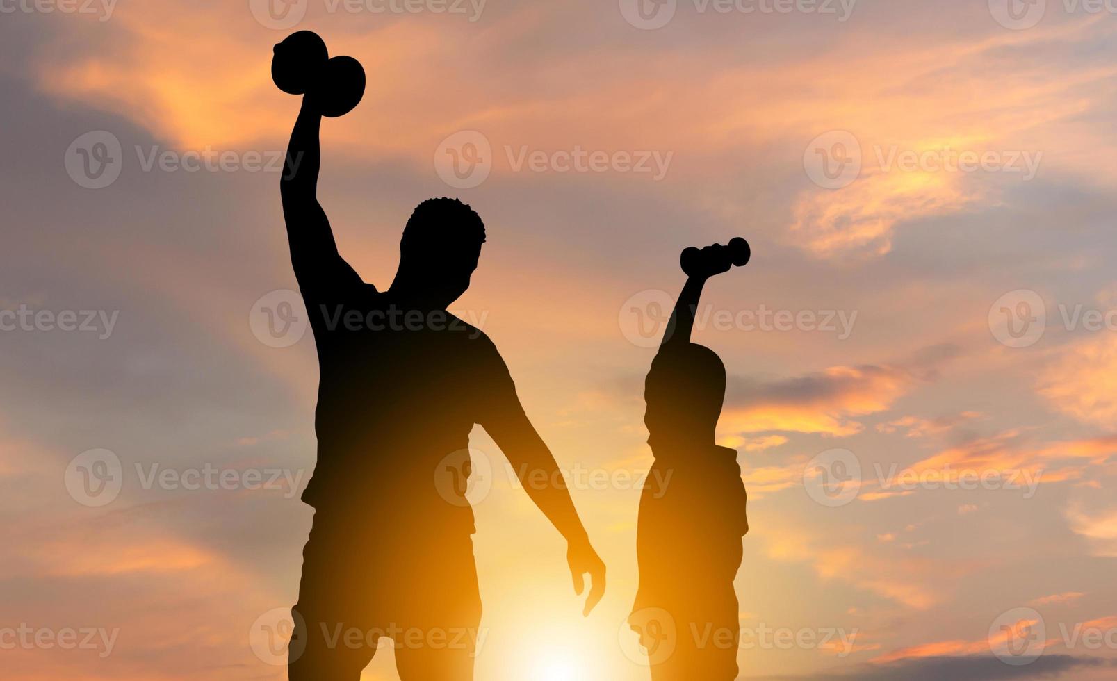 silueta de padre e hijo con un camino recortado jugando a hacer ejercicio con pesas al atardecer, conceptos familiares de felicidad foto