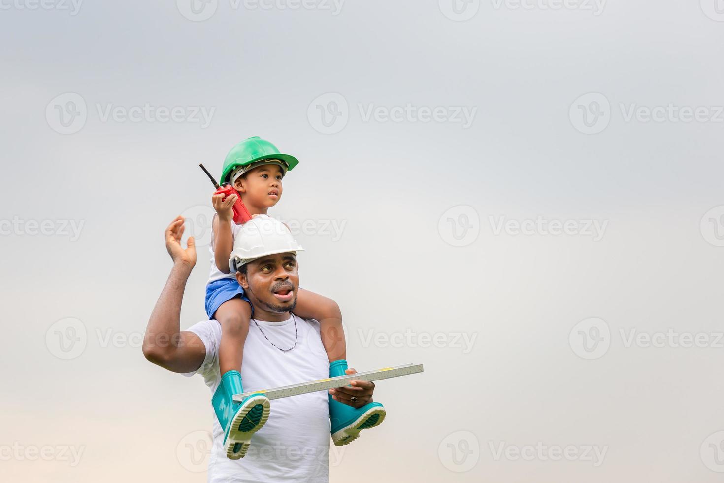 alegre padre afroamericano e hijo con sombrero duro, padre feliz llevando a su hijo sobre los hombros foto