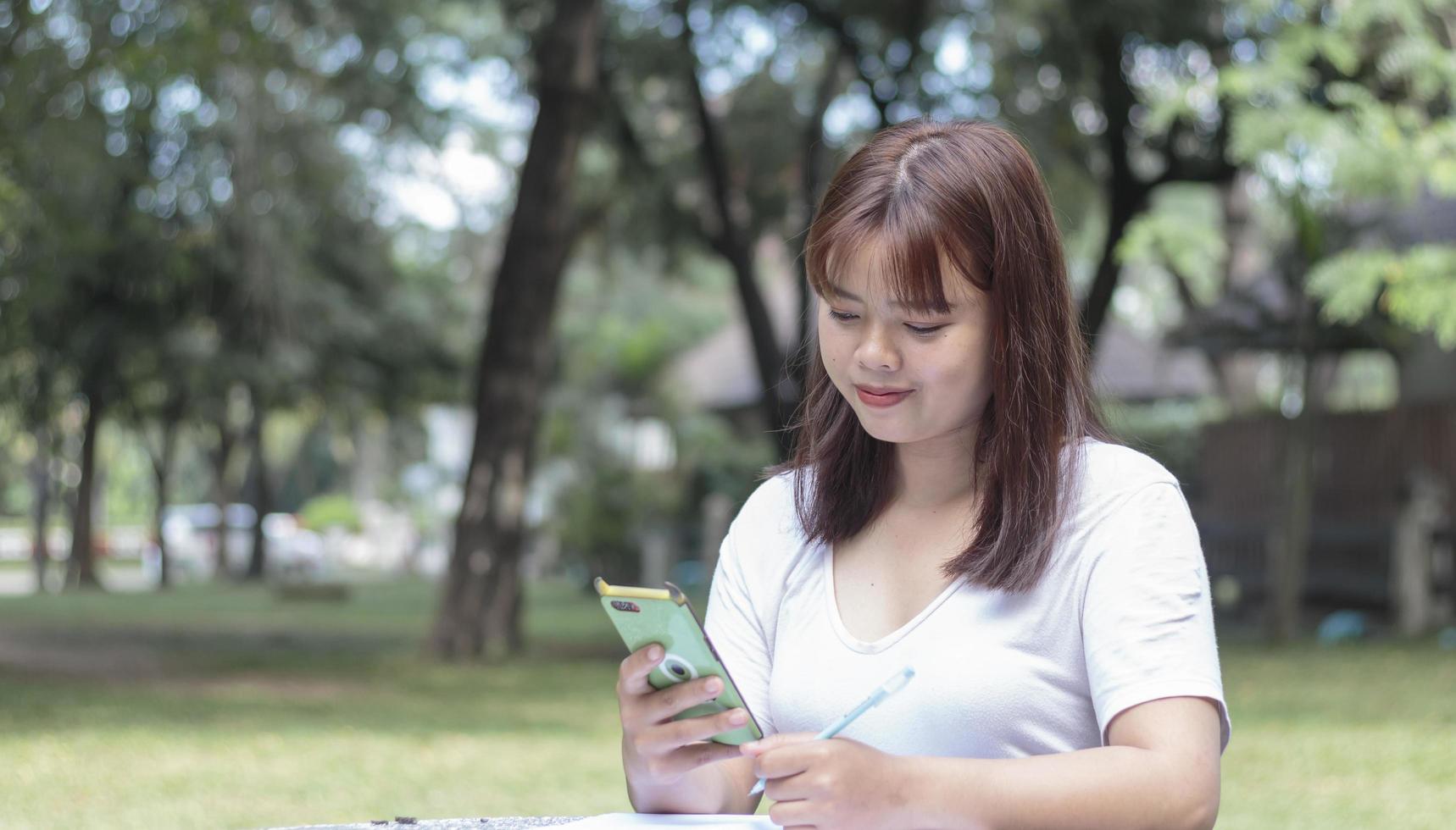 A cute woman is reading a message on her mobile phone while sitting in the park and searching for information on her phone. photo