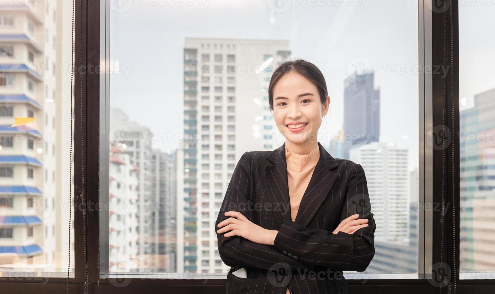 alegre joven mujer de negocios de pie con los brazos cruzados en la oficina foto