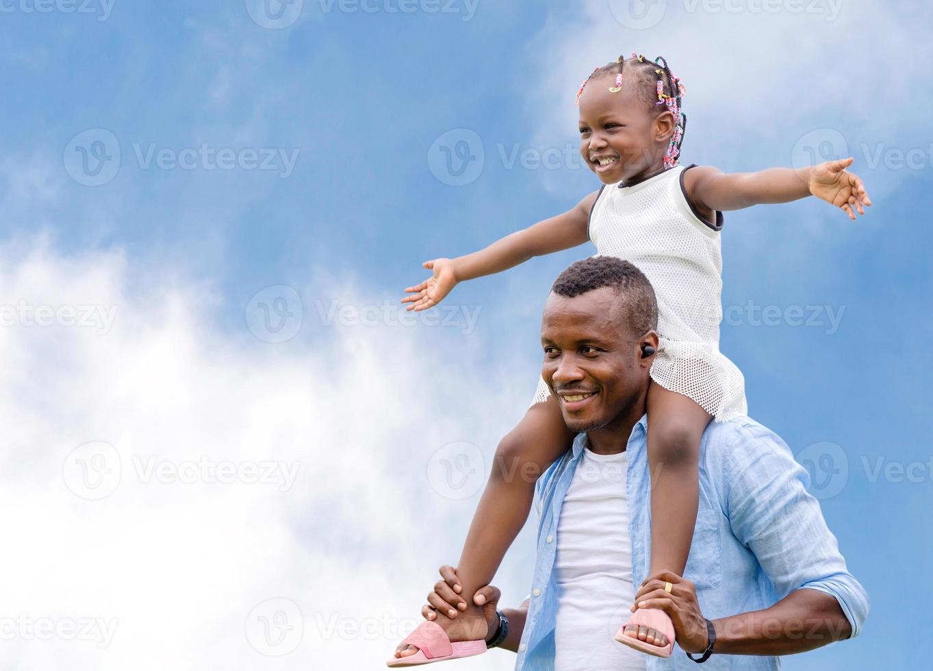 feliz padre cargando a su hija sobre los hombros, alegre niña afroamericana sobre los hombros de su padre con un sendero recortado foto