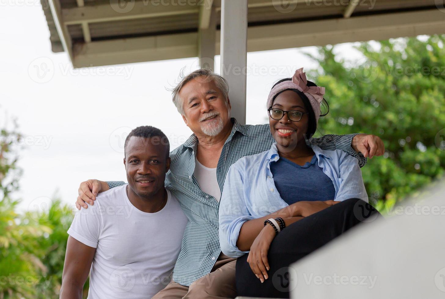 Senior asian man sitting relax with young cheerful african american man and woman at terrace and looking at camera photo