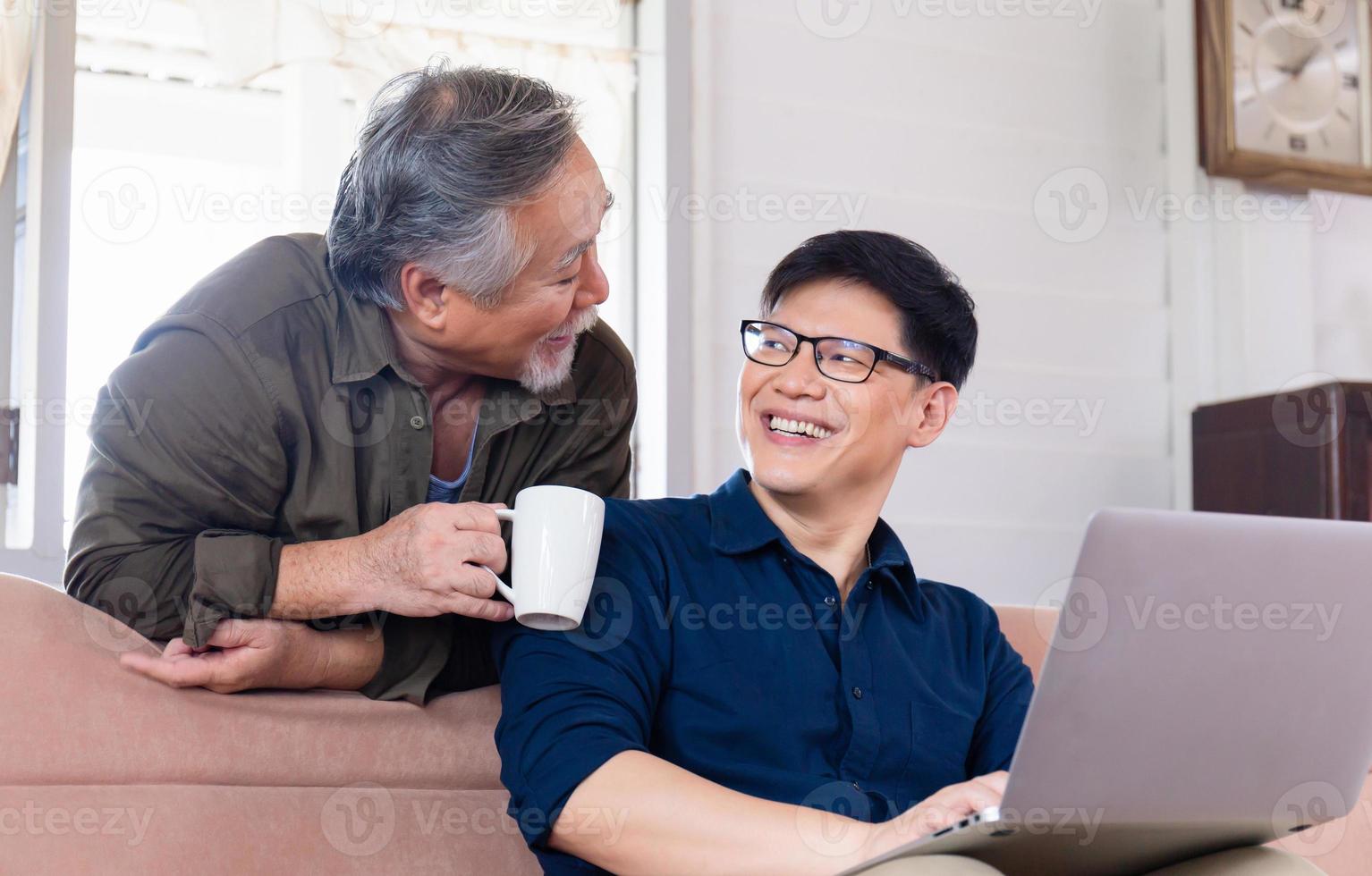 Cheerful old senior mature father and adult son talking conversation at home, Happy asian father and middle aged son using computer laptop in living room photo