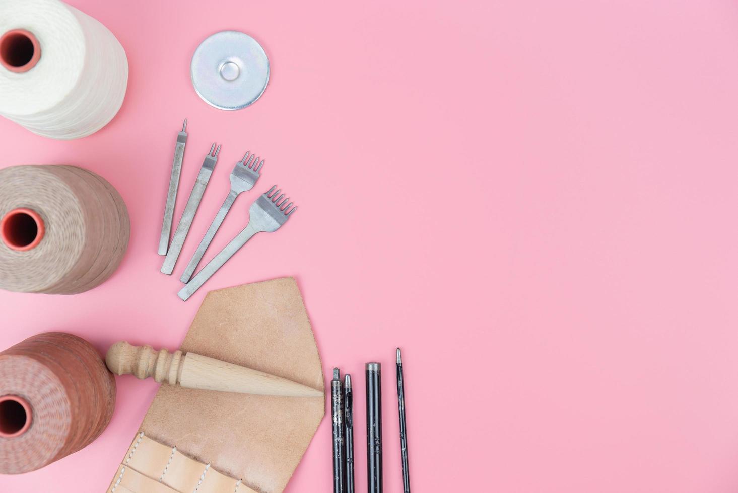 Top view with copy space of leather craft tools group, waxed rope, diamond hole punch and shape punch overhead on pink pastel background, Leather craft or leather working flat lay concept photo