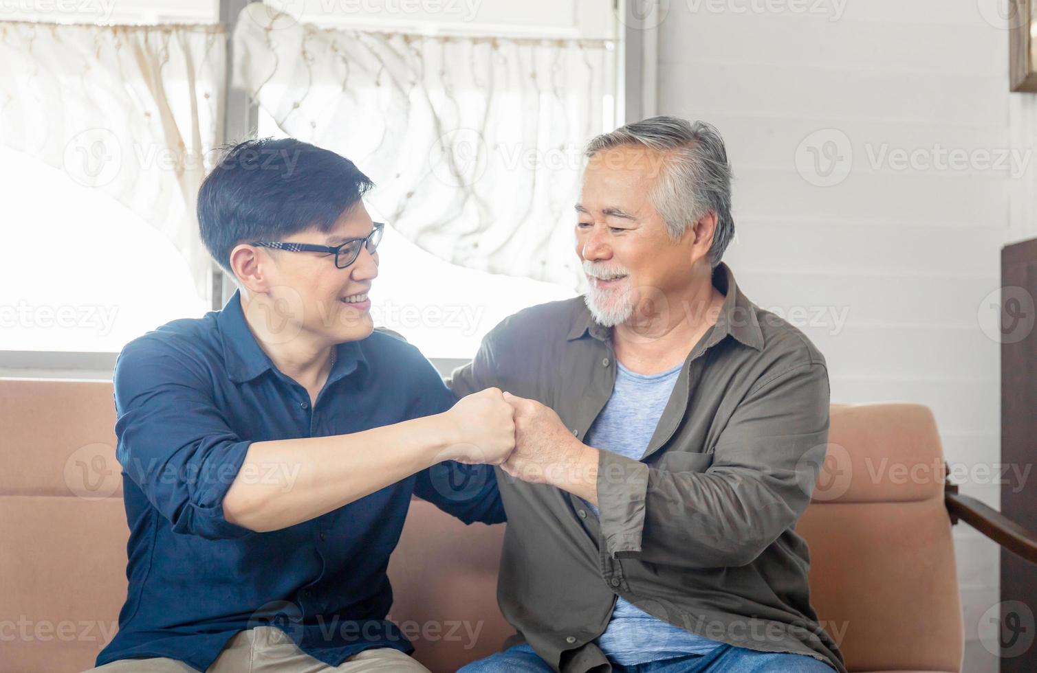 Cheerful senior asian father and middle aged son fists bumping, mature aged dad and millennial man sitting on couch in living room at home, Happiness Asian family concepts photo