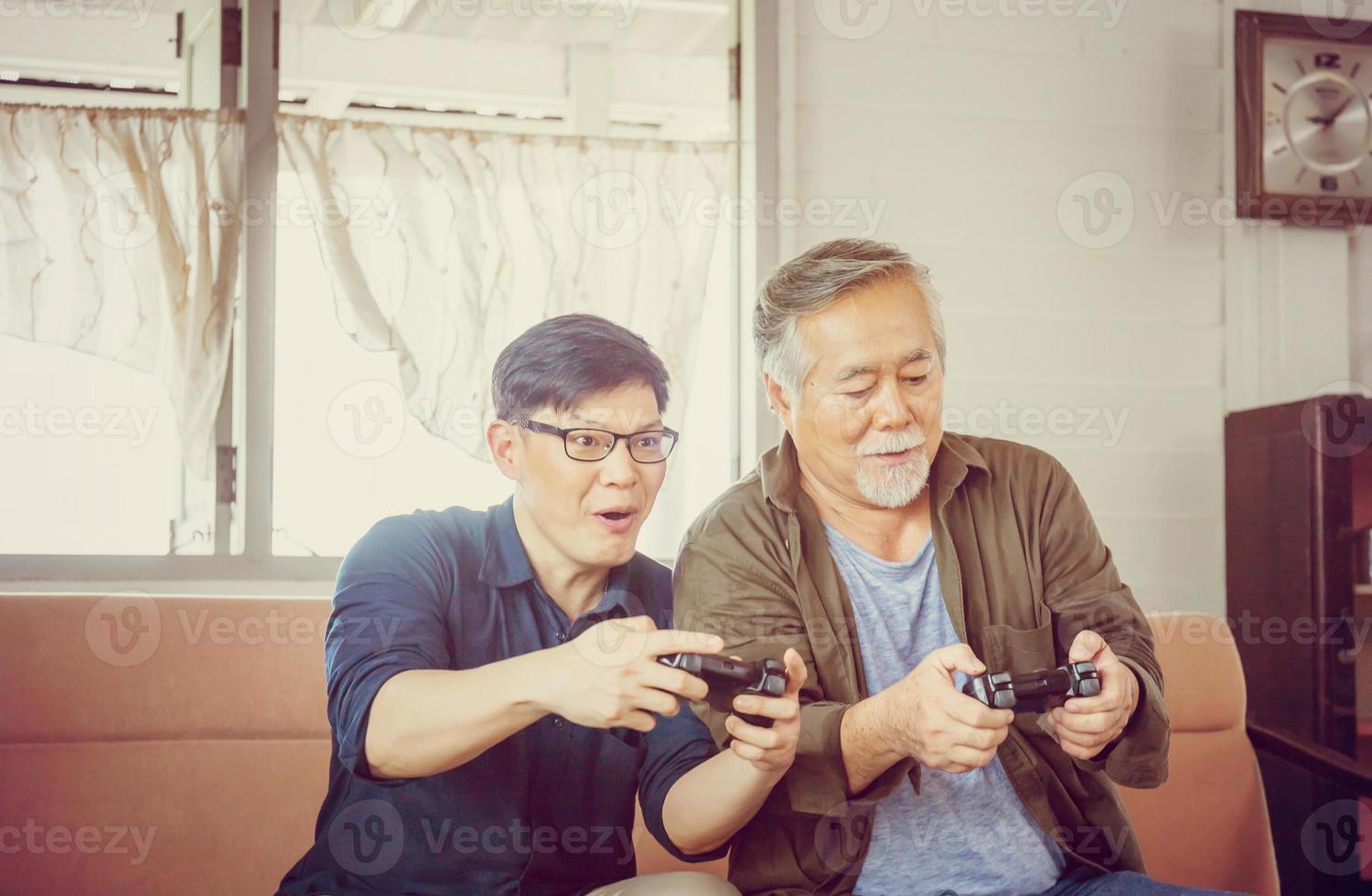 feliz padre asiático senior e hijo de mediana edad jugando videojuegos juntos en la sala de estar, felicidad conceptos familiares asiáticos foto
