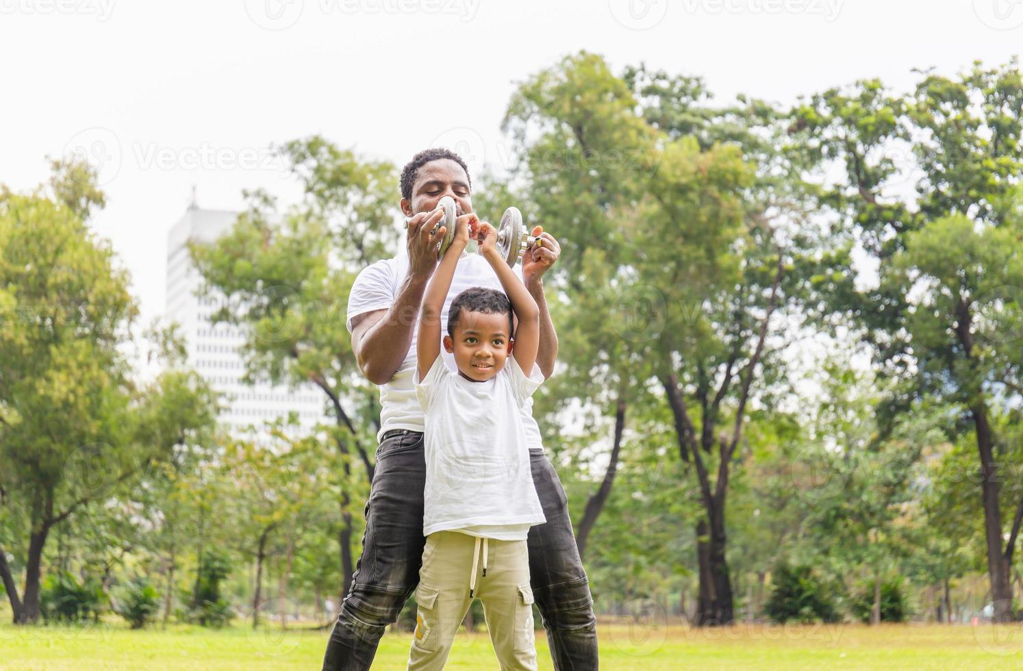 Cheerful african american father and son playing exercising with dumbbell in park, Happiness family concepts photo