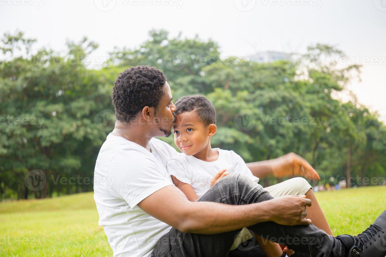 Happy African American father while hug and carry his son, Dad was kissing his son in the park, Joyful black family concept. photo