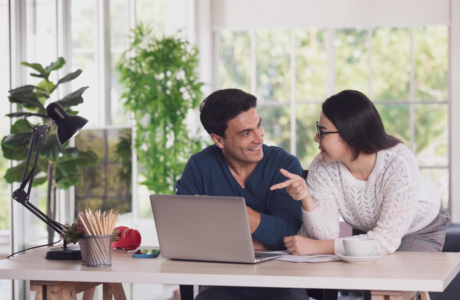 Caucasian man and Asian woman mix race lovers working together via laptop notebook computer and discussing in living room with happy and intimate. New normal work at home office concept photo