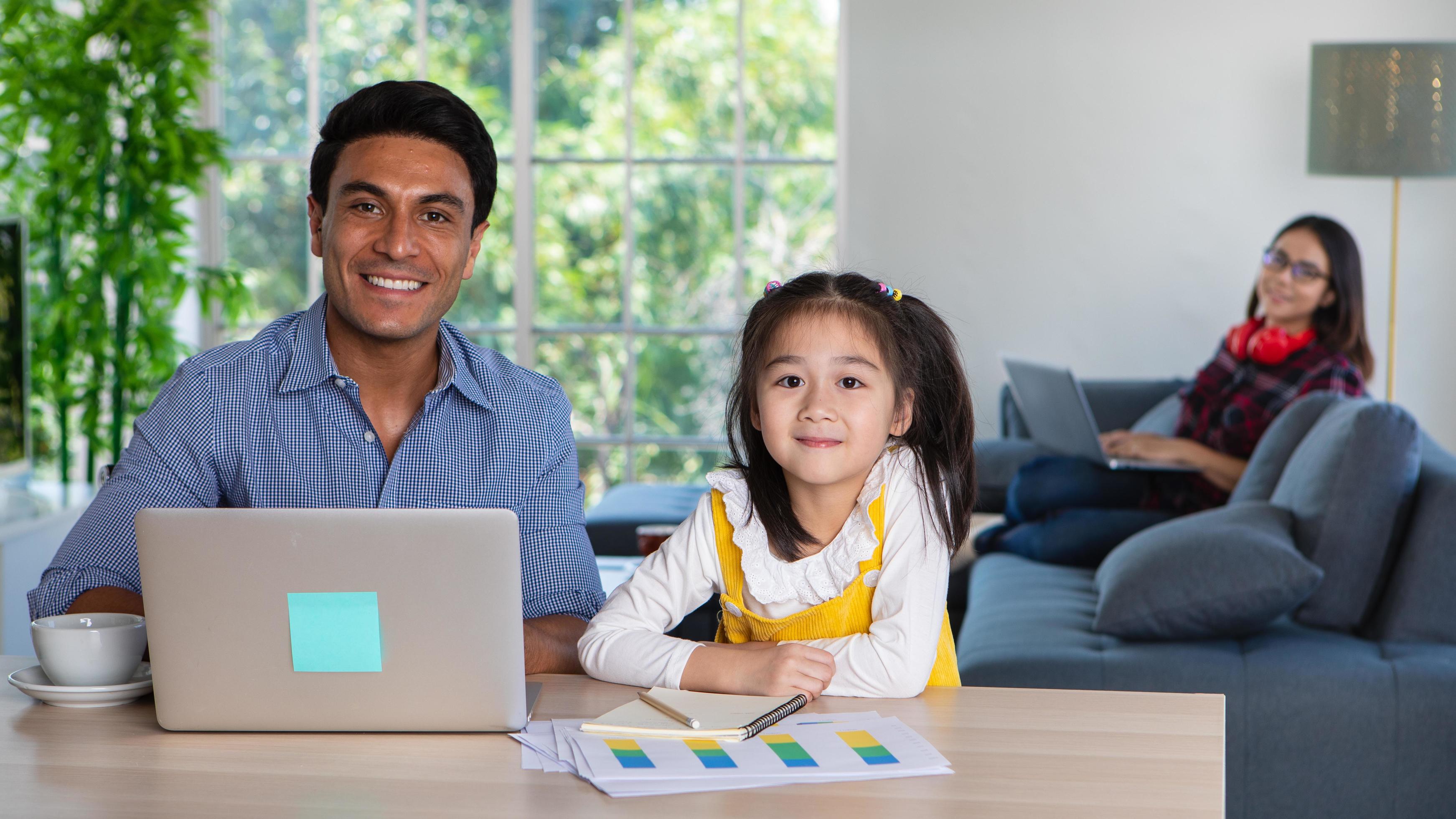 Mixed race sharing time in living room. Caucasian father using computer to work half-Thai girl standing beside him while Asian mother with laptop working her job on sofa 6774562