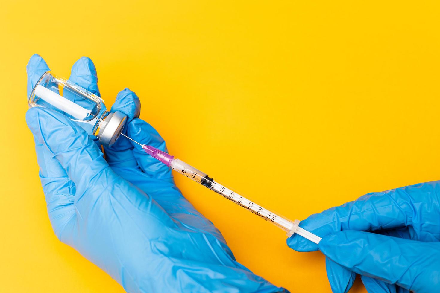 manos con guantes azules sosteniendo una jeringa y apuñalando a una botella de una vacuna sobre fondo naranja con espacio para copiar foto