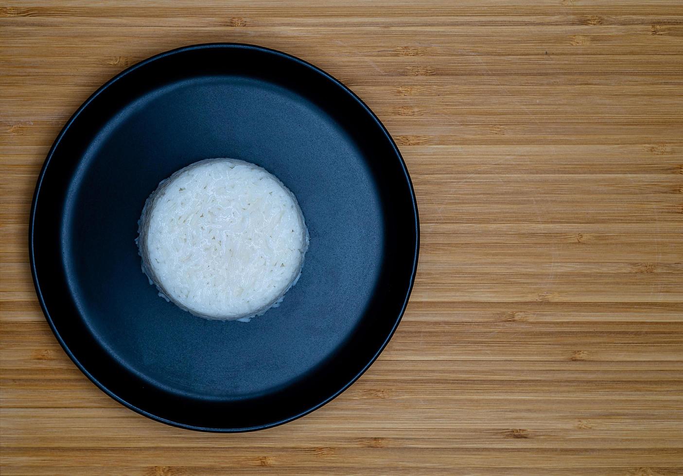 Thai style cooking steam rice put on black plate on wooden background with copy space. Top view angle. photo