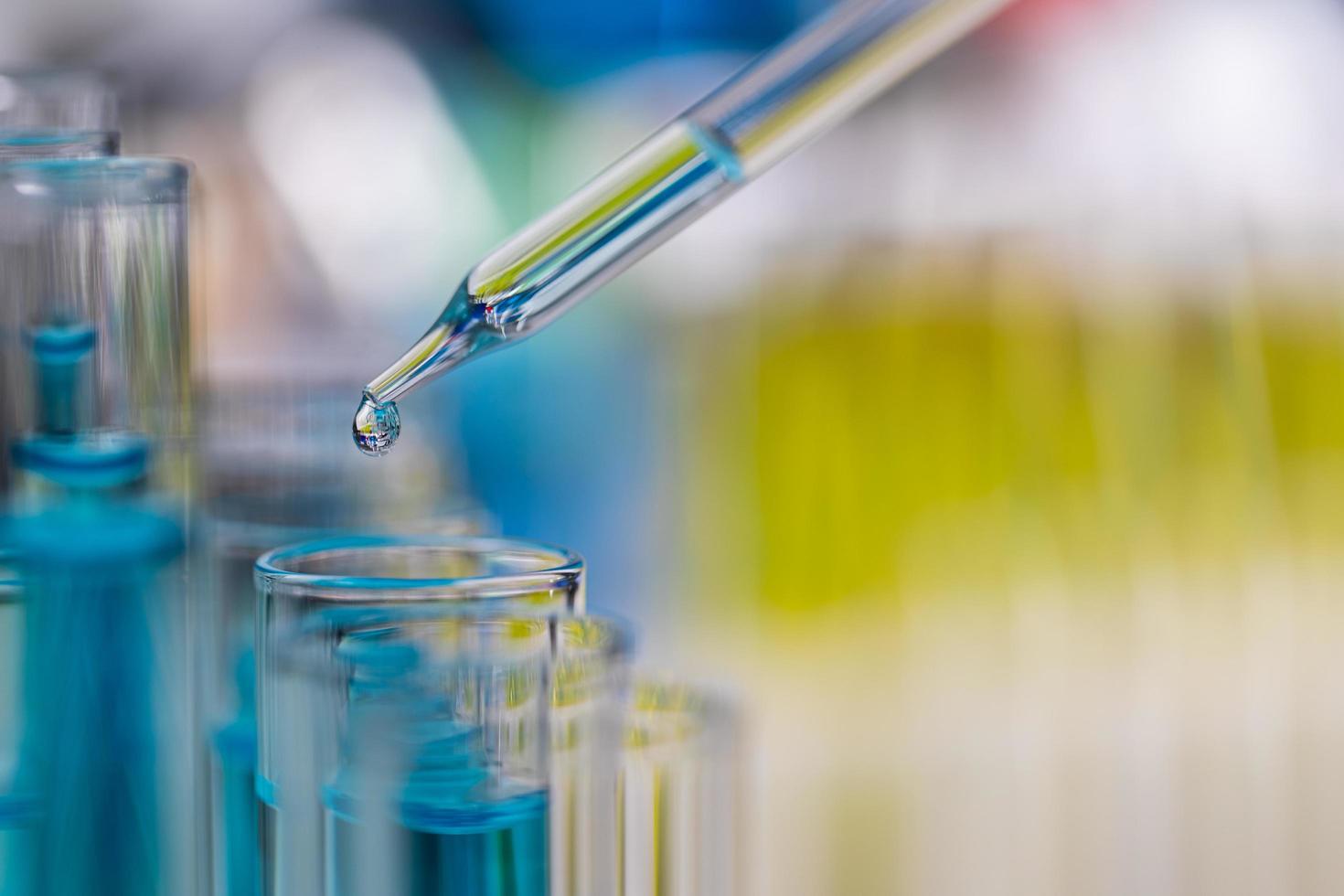 gota de líquido azul del gotero que cae al tubo de ensayo en el laboratorio con un fondo borroso de color brillante foto