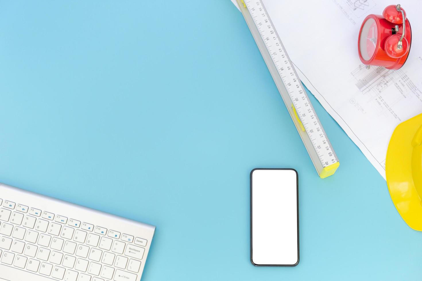 Top view with copy space of Engineering tools, computer keyboard, smartphone, blueprints, helmet, measuring tape overhead on blue pastel background, Flat lay concept photo