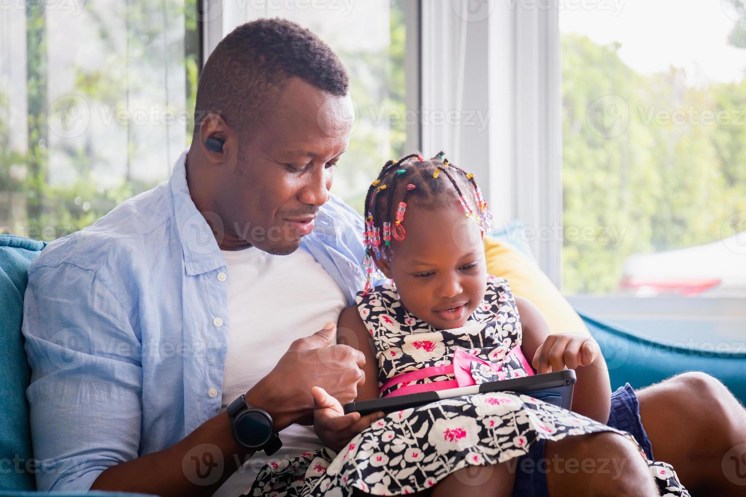 Cheerful african american father and daughter playing in living room, Cute little girl and dad sitting on the sofa and playing on tablet, Happiness family concepts photo