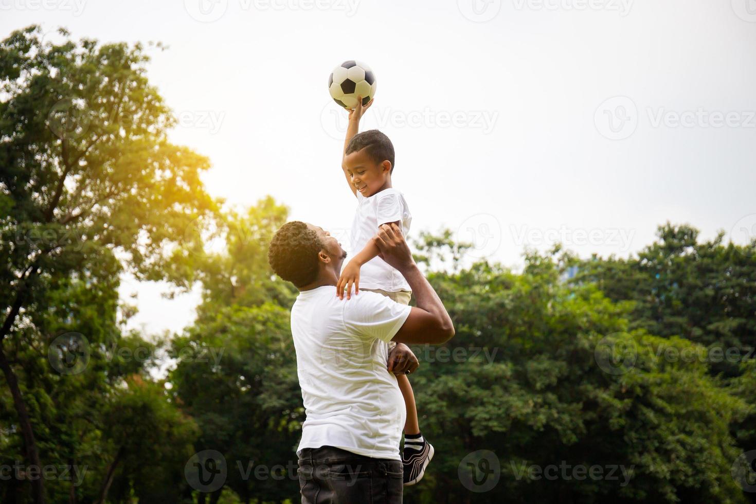 Cheerful african american father and son playing with football in park, Happiness family concepts photo