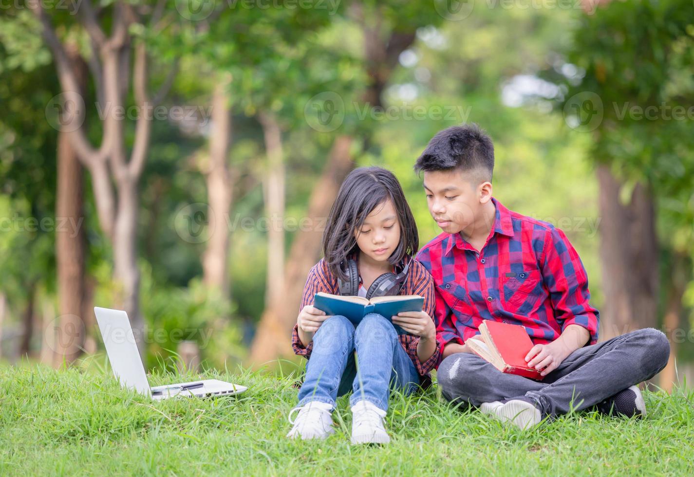 Brother and sister sitting on the grass and reading the book in the park, Kids playing Outdoor learning concept photo