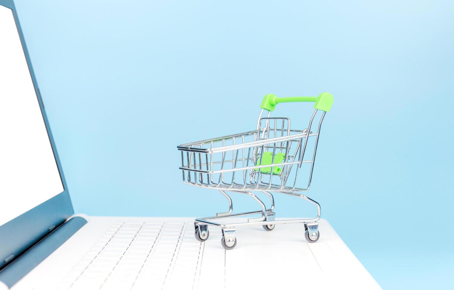 Shopping cart on white laptop pc with light blue background, Online shopping concepts photo