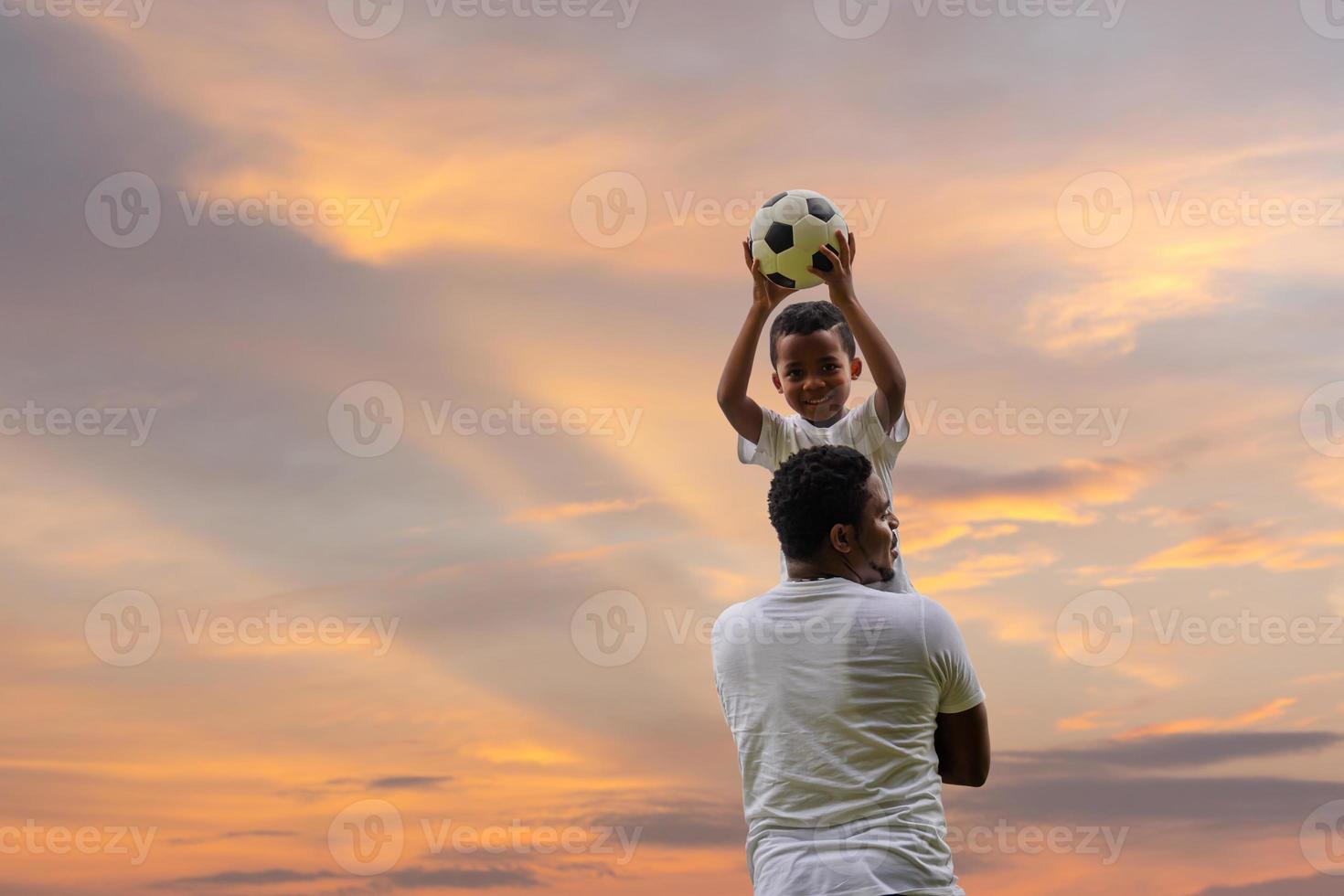 alegre padre afroamericano e hijo jugando al fútbol al aire libre, conceptos familiares de felicidad foto