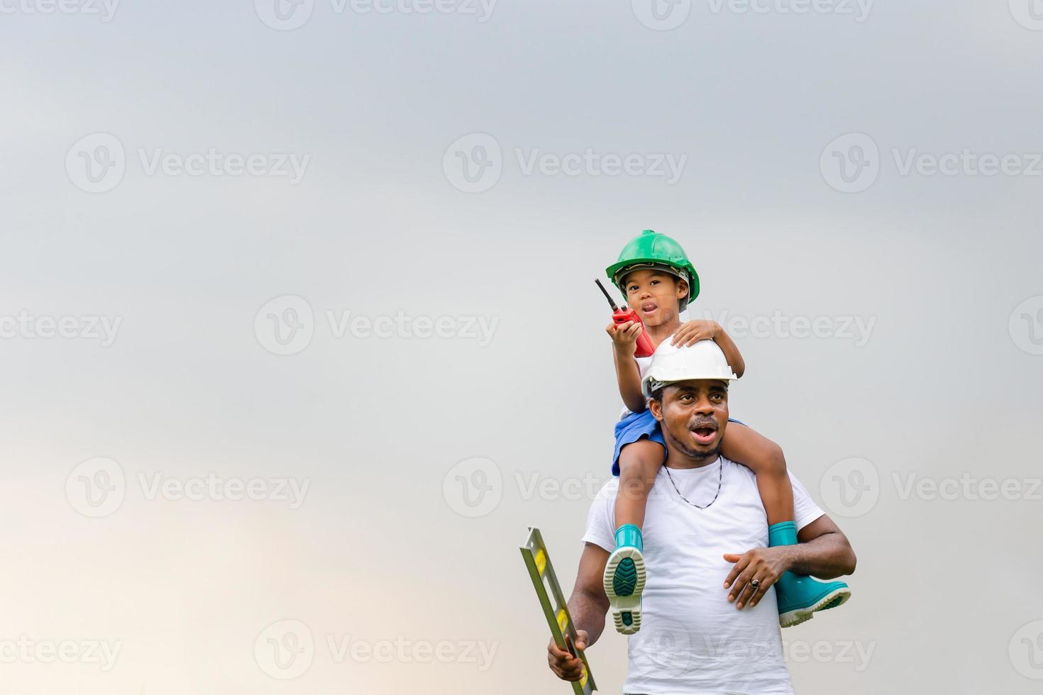 Cheerful african american father and son in hard hat, Happy dad carrying son on shoulders photo