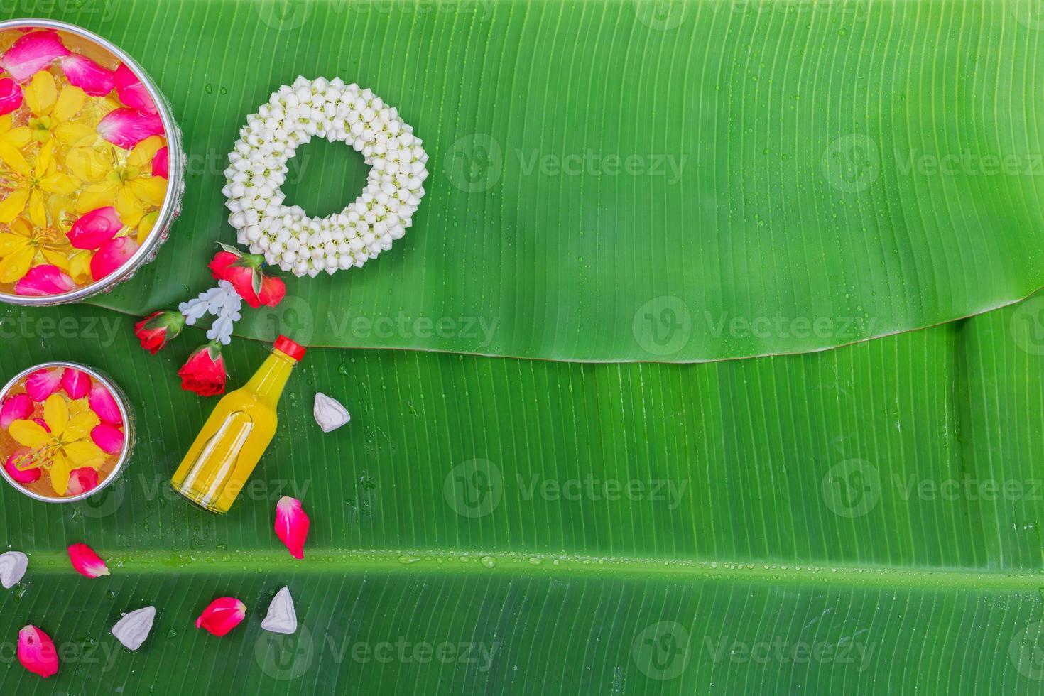 Songkran Festival background with jasmine garland Flowers in a bowl of water, perfume and limestone on a green wet banana leaf background. photo